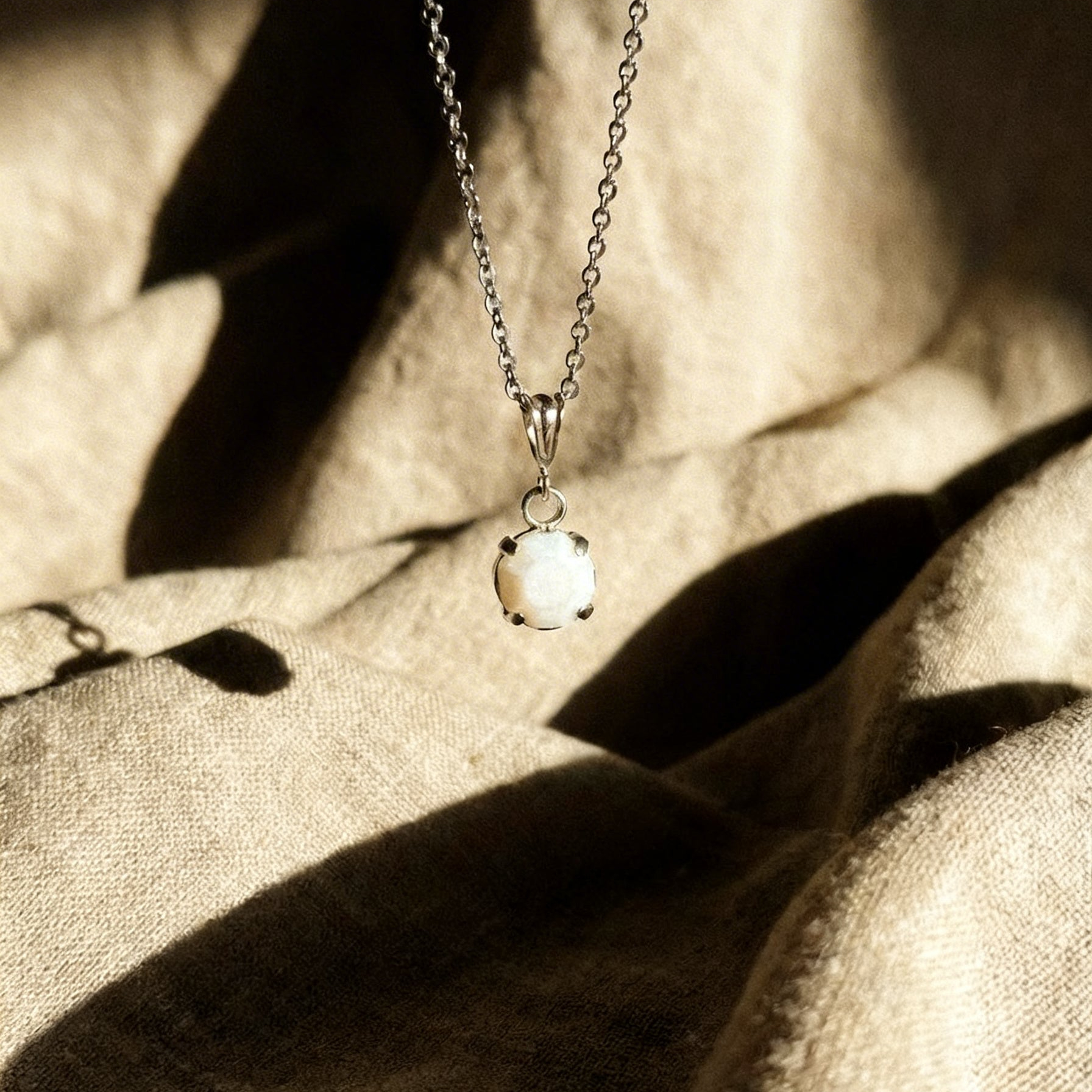 Collana Cabochon in argento con gemma bianca opaca, su tessuto di lino